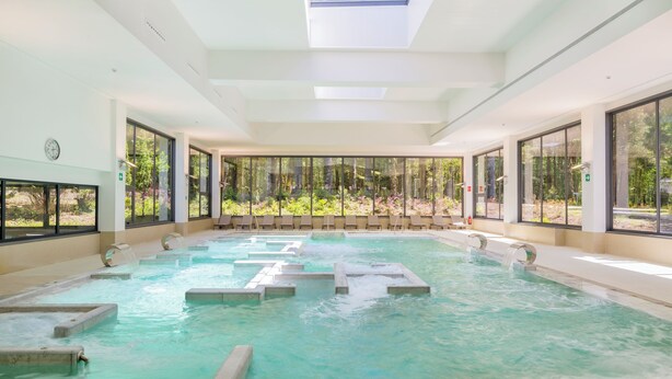 Une grande piscine intérieure à l’eau claire, entourée de grandes fenêtres qui offrent une vue sur la verdure.