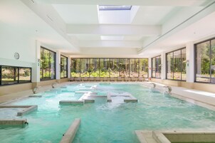 A large indoor swimming pool with clear water, surrounded by large windows offering views of greenery.
