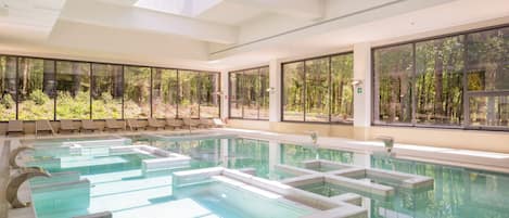 Piscina interior moderna com paredes de vidro transparente, várias pistas e ambiente iluminado pelo sol.
