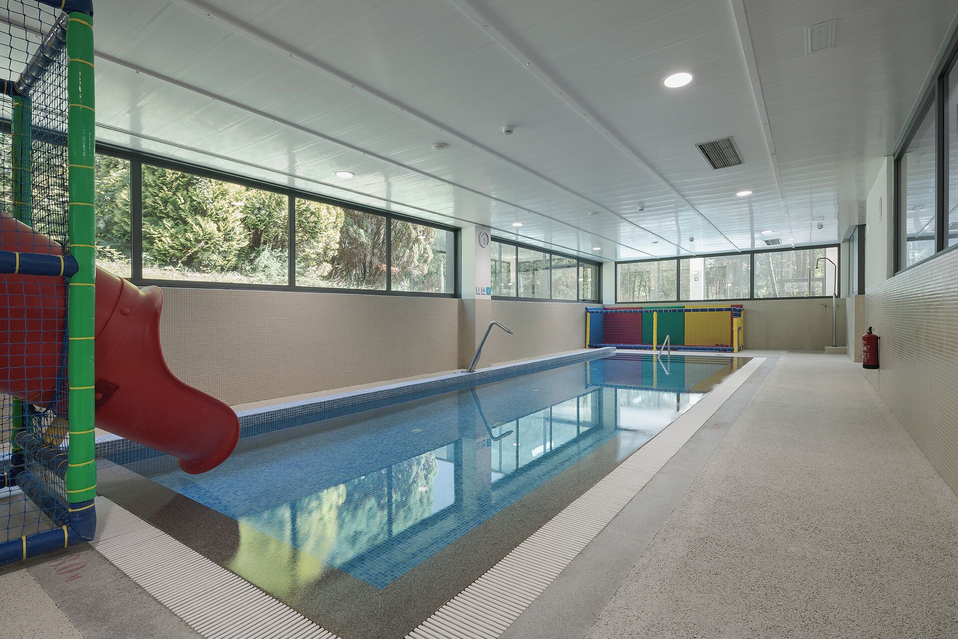 Una piscina interior con tobogán, barreras de seguridad y extintor.