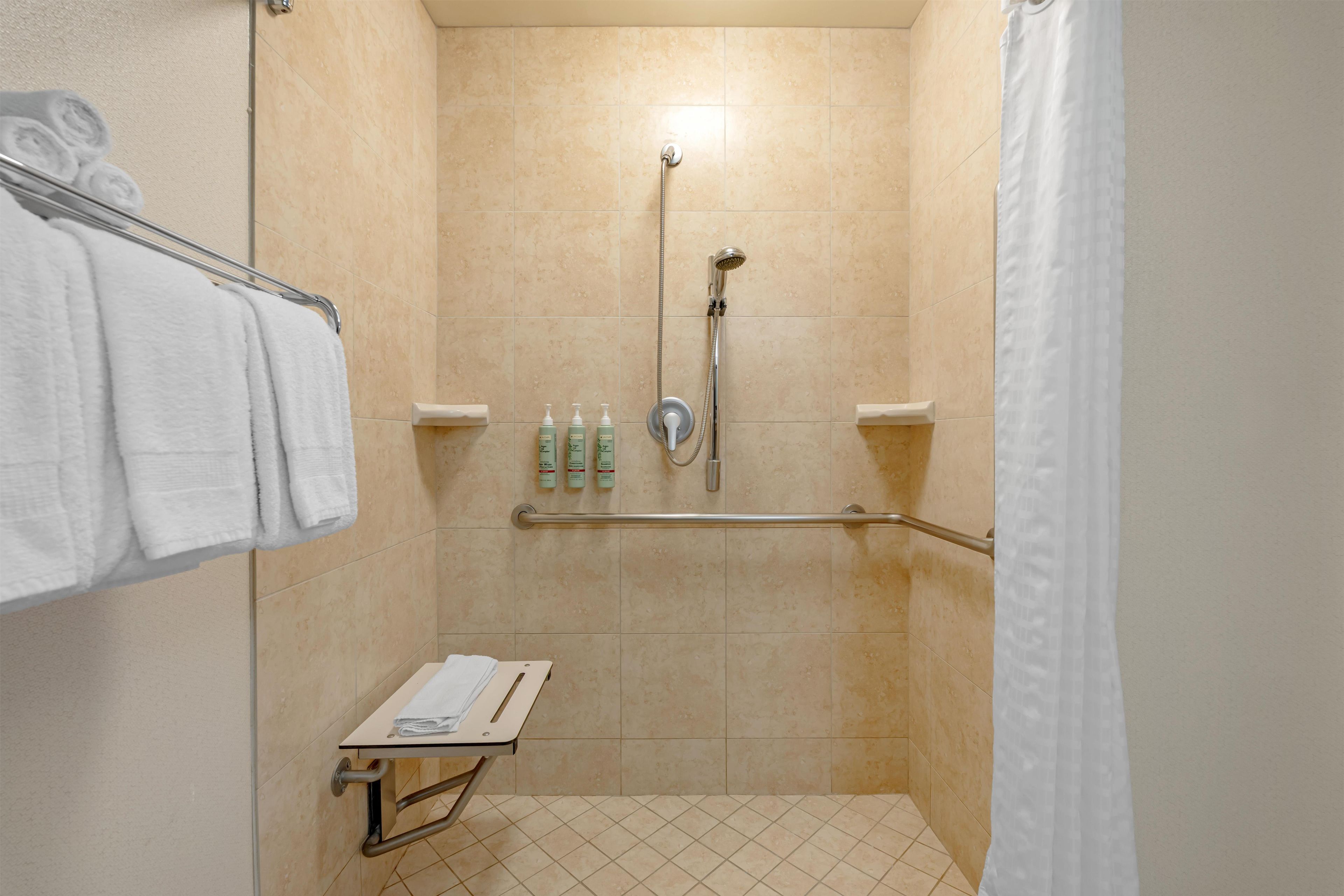 A shower stall with a grab bar, a towel rack, and a shelf with toiletries.