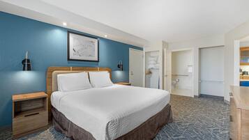 Ein Hotelzimmer mit einem großen Bett, einem Nachttisch, einer Wandleuchte, einem gerahmten Bild und einem durch eine offene Tür einsehbaren Badezimmer.