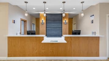 Un comptoir d’accueil avec un revêtement en bois, deux écrans d’ordinateur et des luminaires suspendus.