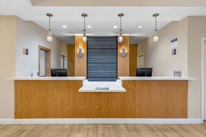 Un mostrador de recepción con detalles de madera, dos monitores de computadora e iluminación colgante.