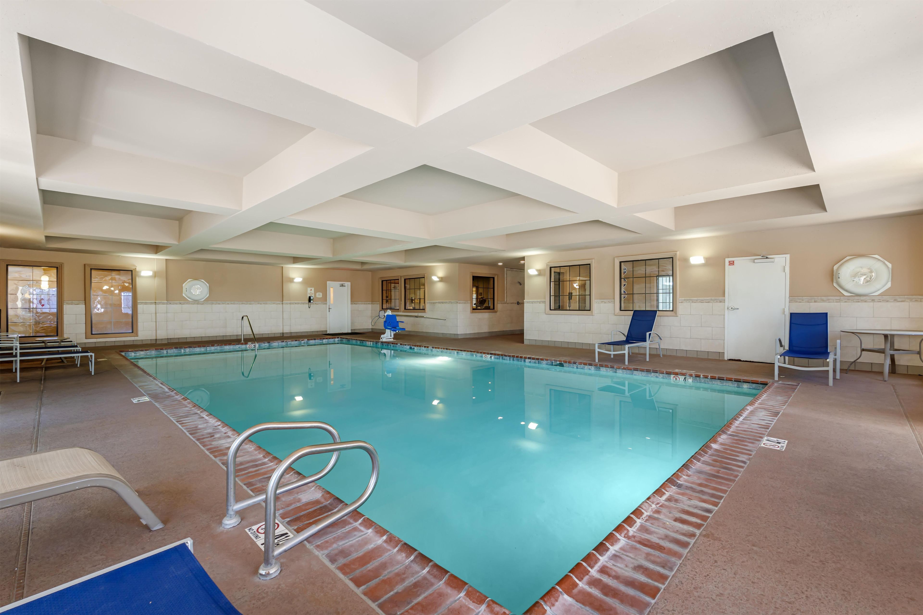 An indoor swimming pool with clear water, a diving board, and a few lounge chairs.