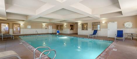 An indoor swimming pool with clear water, a diving board, and a few lounge chairs.
