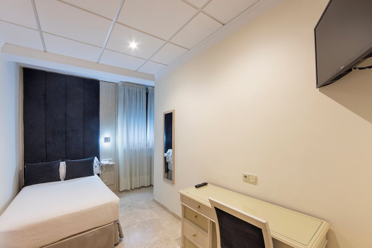 A hotel room with a bed, a desk, a mirror, and a TV mounted on the wall.