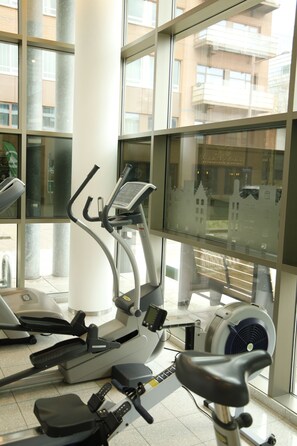 A gym with exercise equipment, large windows, and a view of buildings outside.
