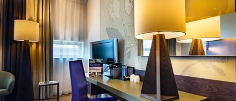 A hotel room with a desk, a chair, a television, and a lamp.