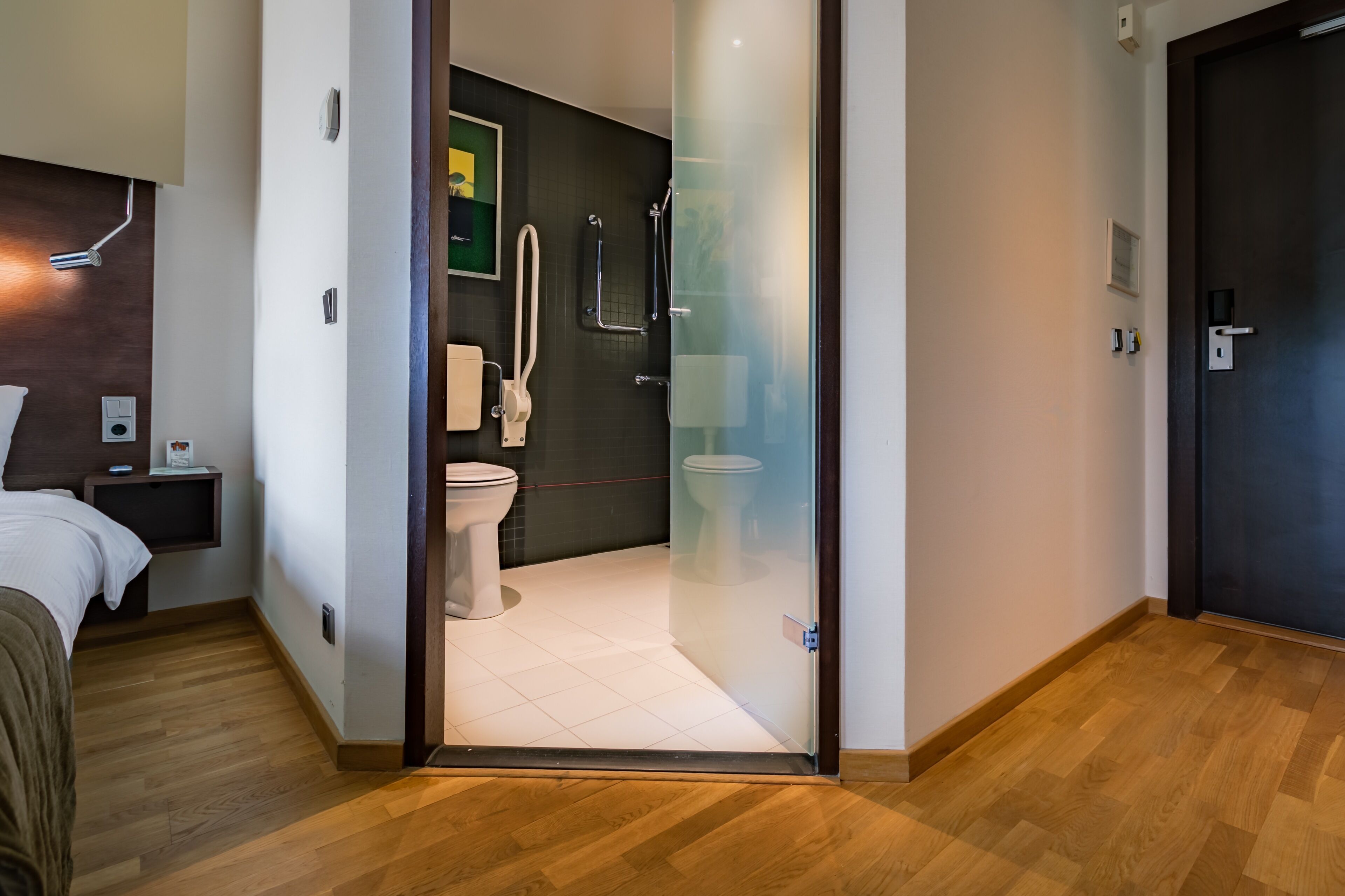 A modern bathroom with a toilet, shower, and glass door leading to a bedroom.