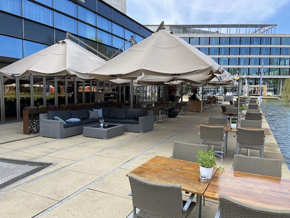 An outdoor seating area with wicker furniture, umbrellas, and a view of a modern building.
