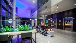 A modern lobby with a long reception desk, seating area, and elevators. - Hotel Artemis Amsterdam (Amsterdam)