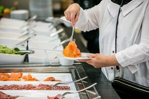 A buffet with various food items including sliced meats and a person serving themselves.