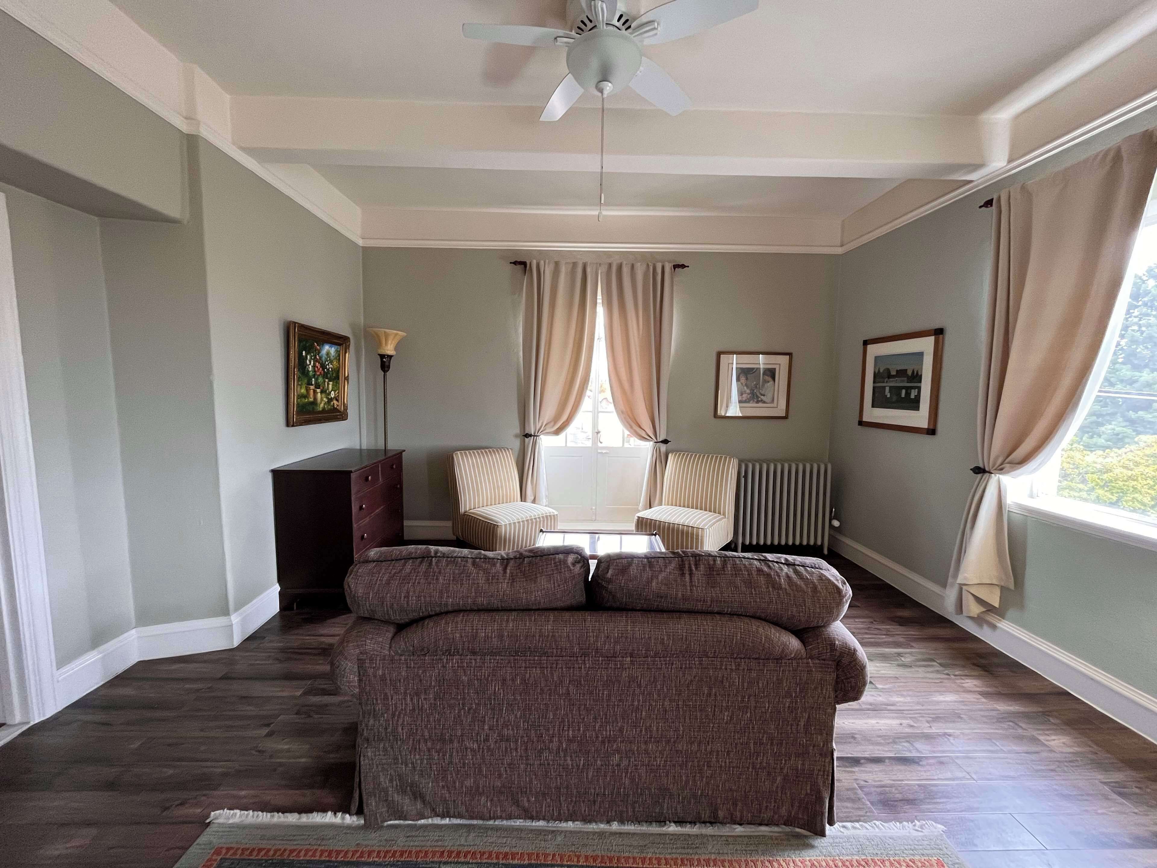 Quarto com sofá, cadeira, radiador e janela com cortinas.