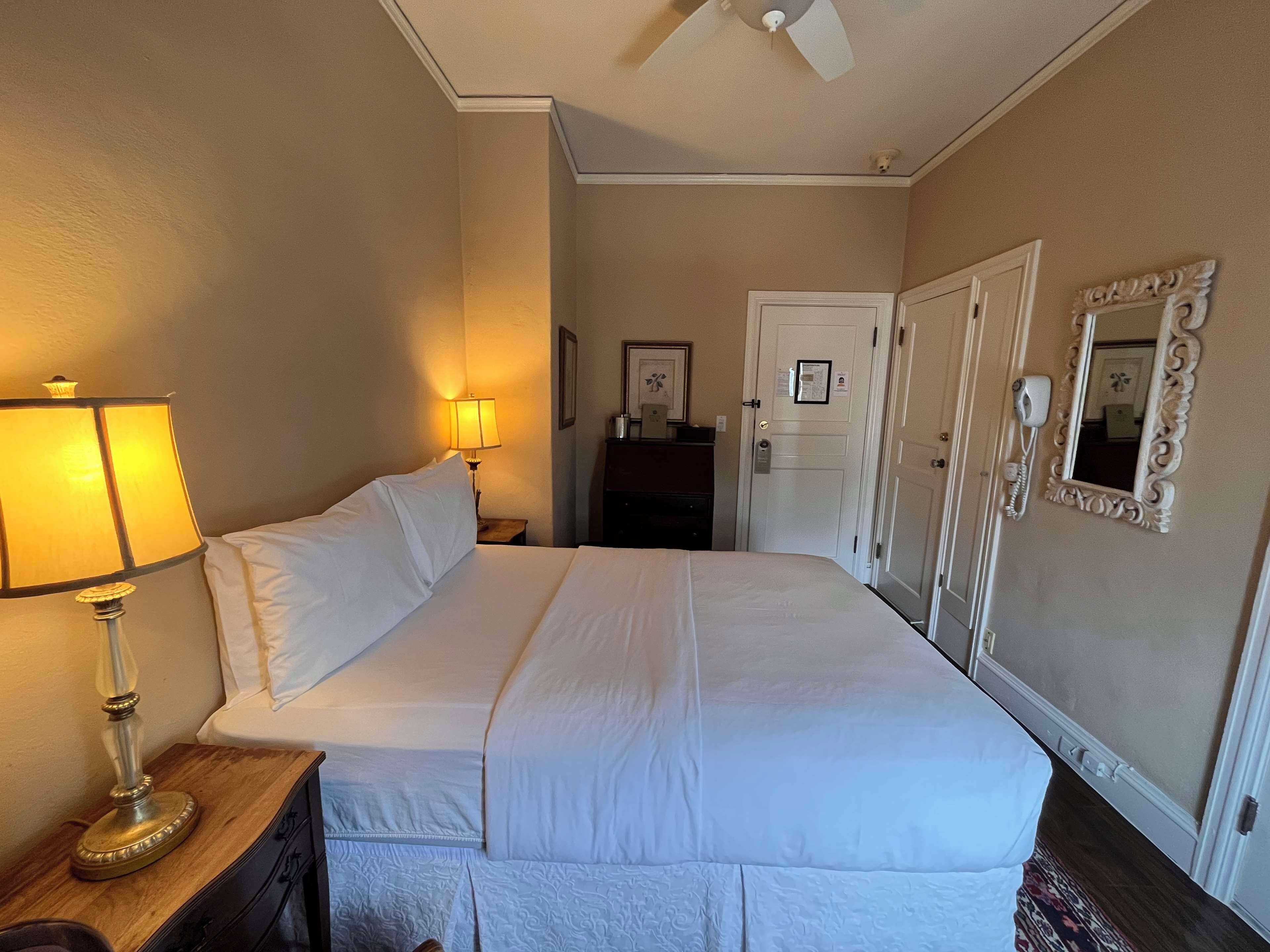 Hotelkamer met een groot bed, twee bedlampen, een plafondventilator, een deur met spiegel en een telefoon.
