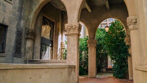 An architectural corridor with arches and columns, a window with a metal grille, and a view of a garden with a lamp post. - Berkeley City Club (Berkeley)