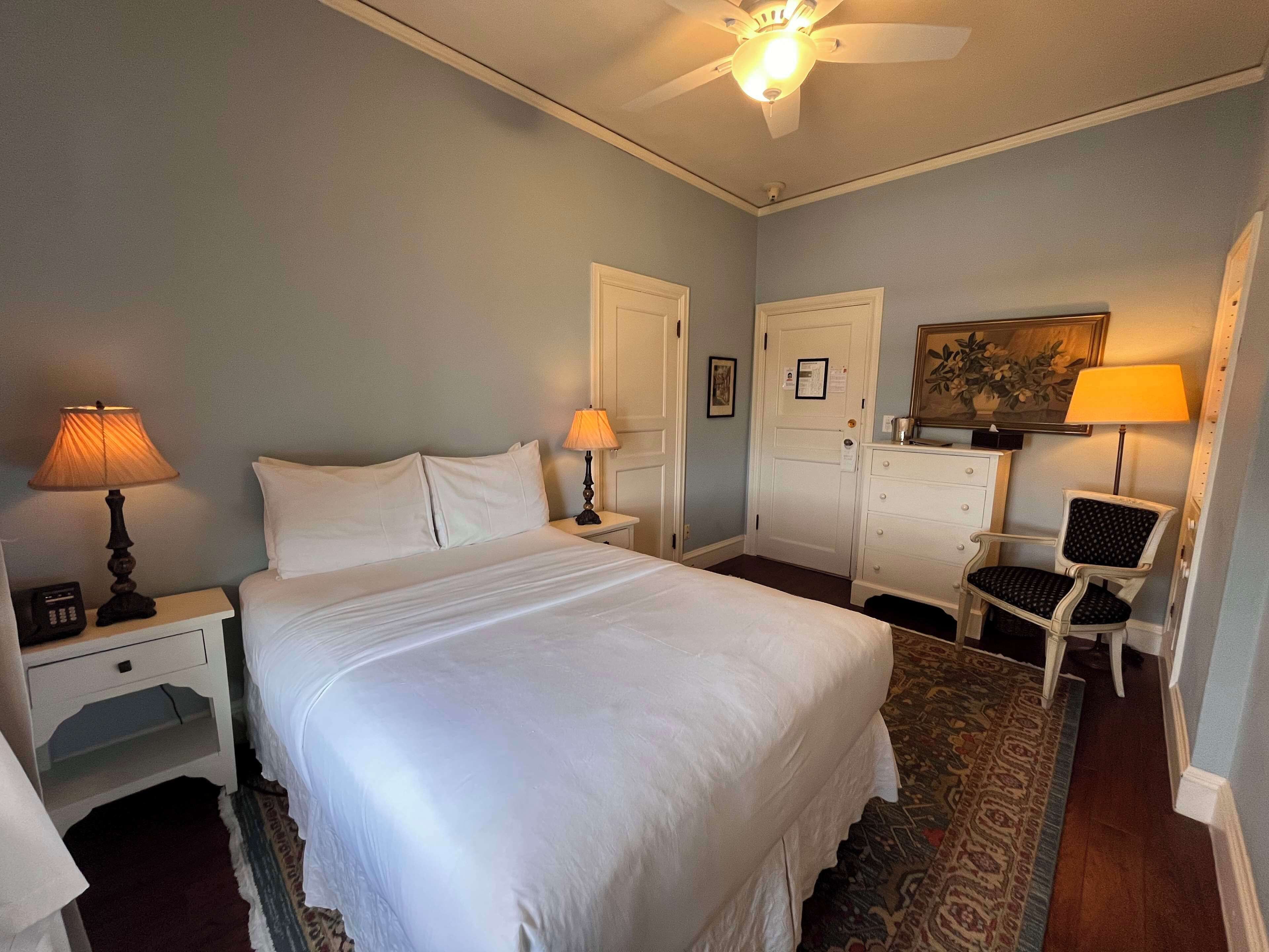 A neatly arranged bedroom with a large bed, two bedside tables with lamps, a dresser, and a chair.