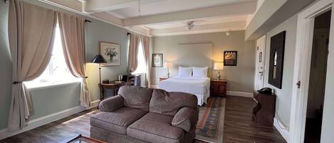 Een ruime slaapkamer met een groot bed, een zithoek met een bank, een glazen salontafel en een plafondventilator.