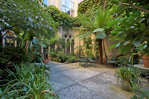 A courtyard with a stone floor, surrounded by lush greenery and potted plants.