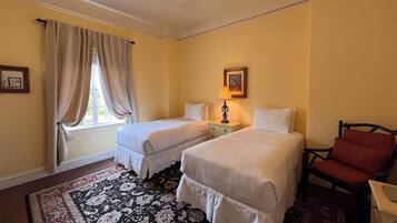 Une chambre d’hôtel avec deux lits, un bureau, une chaise, un ventilateur de plafond et une fenêtre avec des rideaux.