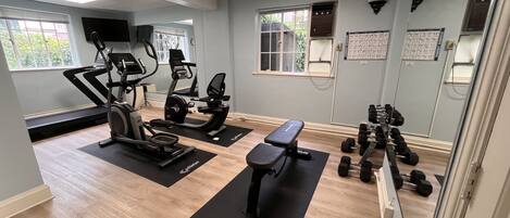 A gym with treadmills, stationary bikes, a bench, and dumbbells.