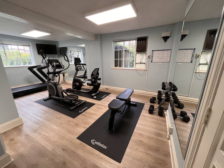 A gym with treadmills, stationary bikes, a bench, and dumbbells.