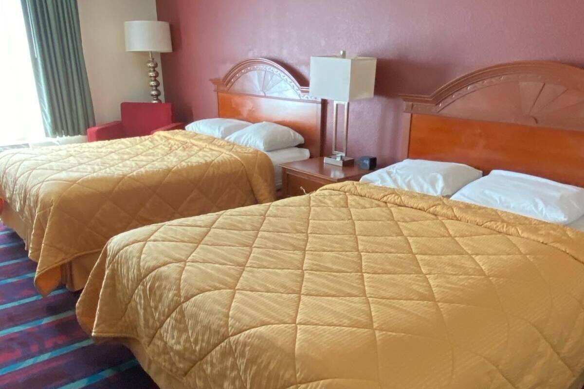 A hotel room with two beds, each with a quilted bedspread, a nightstand with a lamp, and a window with curtains.