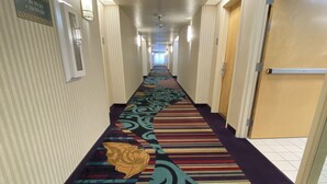 A hotel hallway with a patterned carpet, a fire exit sign, and a door on the right. - Budget Inn San Leandro (San Leandro)
