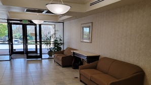 A lobby with a brown sofa, a reception desk, a hanging light fixture, and a framed picture on the wall. - Budget Inn San Leandro (San Leandro)