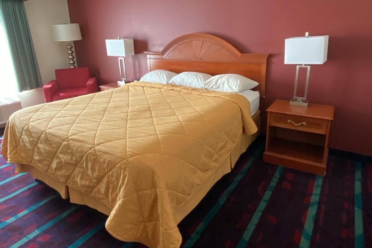 A hotel room with a bed, two bedside lamps, a red chair, and a patterned carpet.