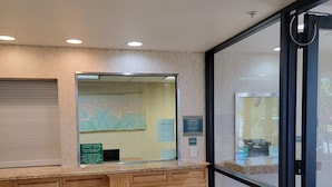 A reception desk with a glass partition, a bulletin board with notices, and a view of the lobby area. - Budget Inn San Leandro (San Leandro)