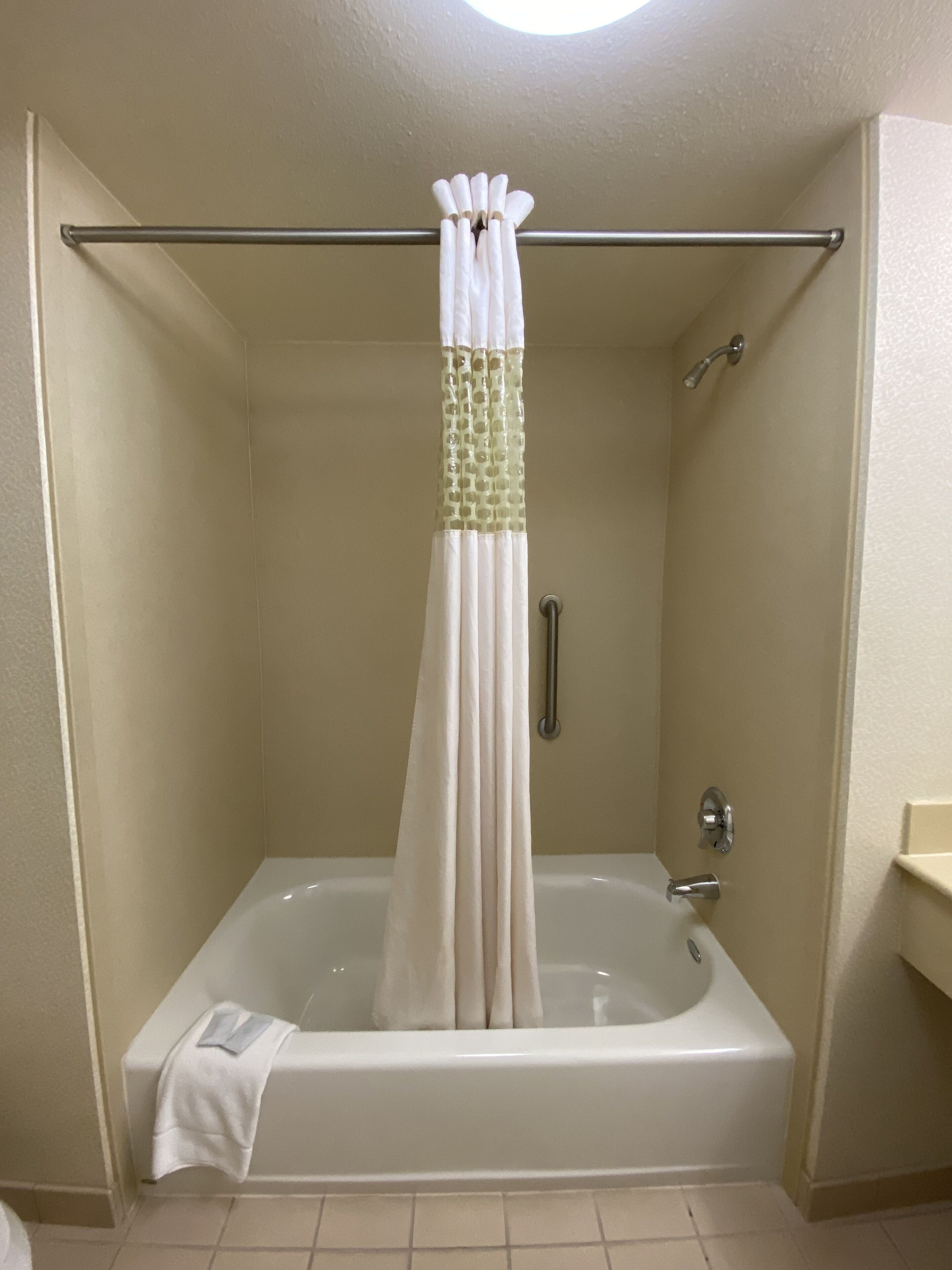 A bathroom with a bathtub, a shower curtain, and a towel on the floor.