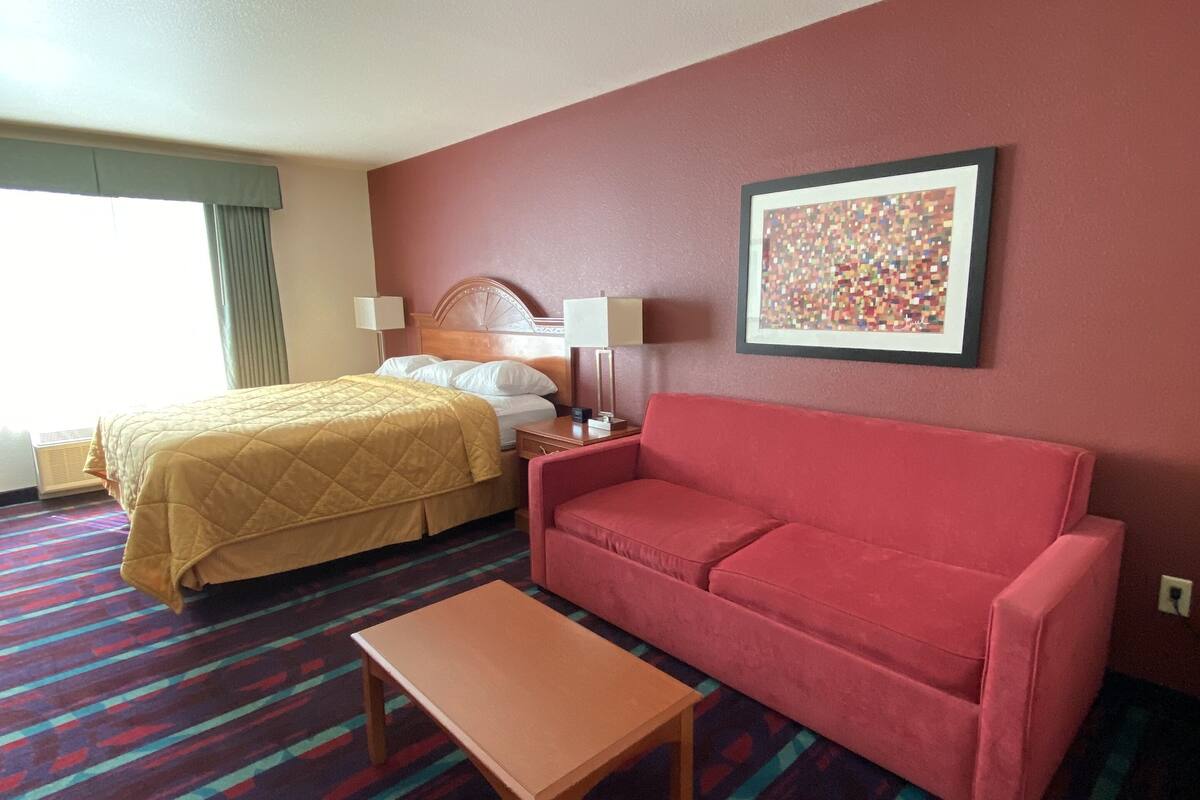 A hotel room with a bed, a red sofa, a wooden table, and a patterned carpet.