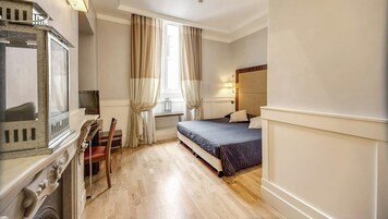 Una habitación de hotel con una cama, un escritorio con televisor y una ventana con cortinas.