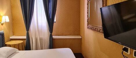Habitación de hotel con una cama grande, un televisor de pantalla plana montado en la pared y una ventana con cortinas.