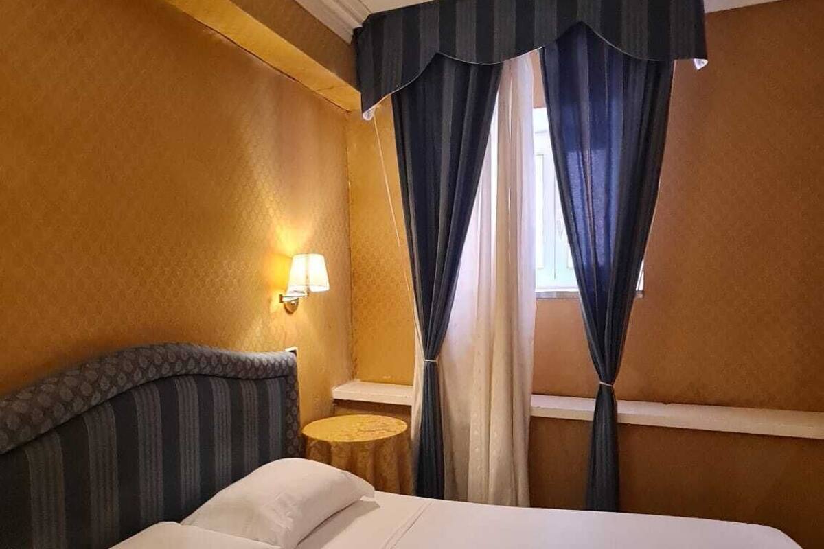 Hotellihuone, jossa on suuri sänky, yöpöytälamppu ja ikkuna, jossa on verhot.