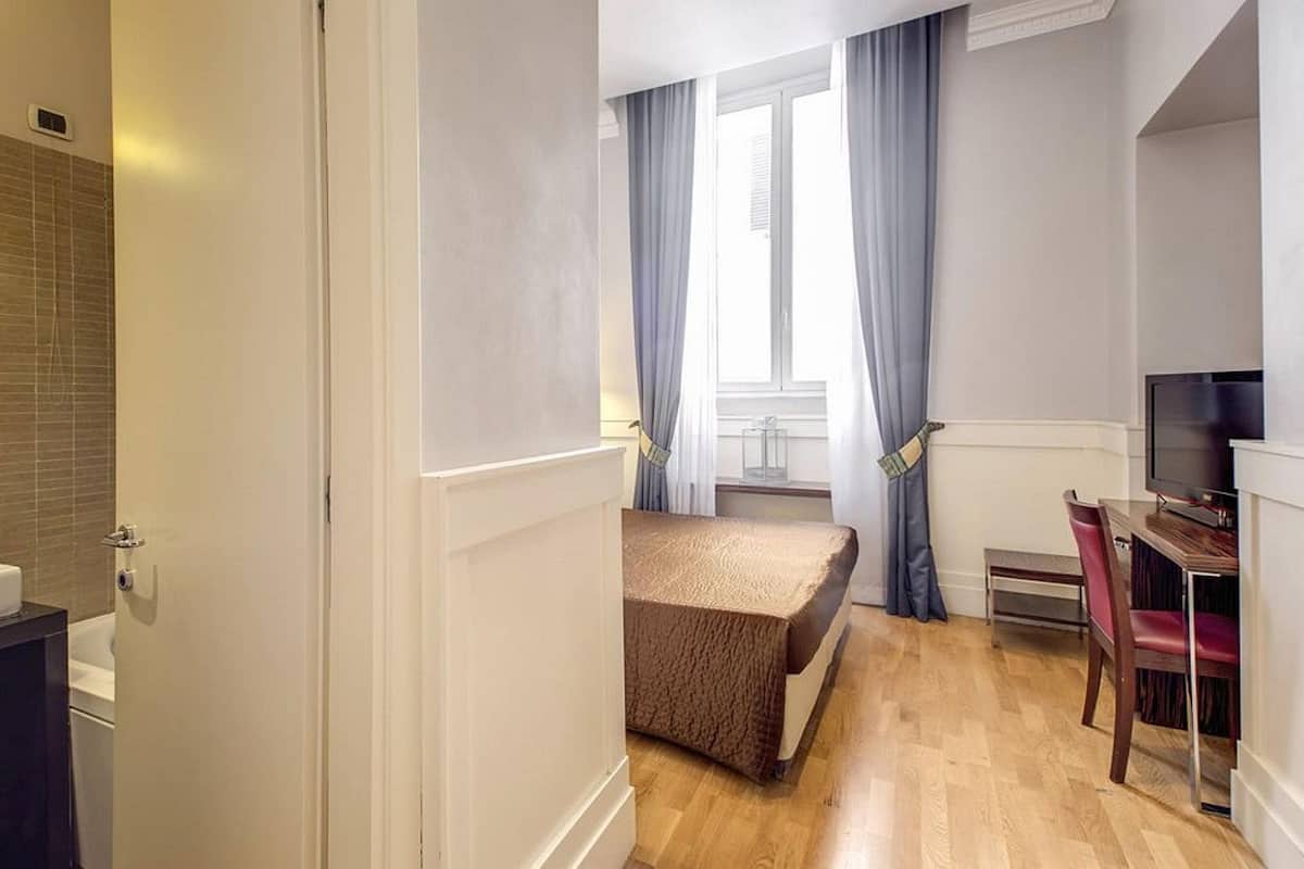 Pieni hotellihuone, jossa on kylpyhuone, sänky, työpöytä tuolilla ja televisio.
