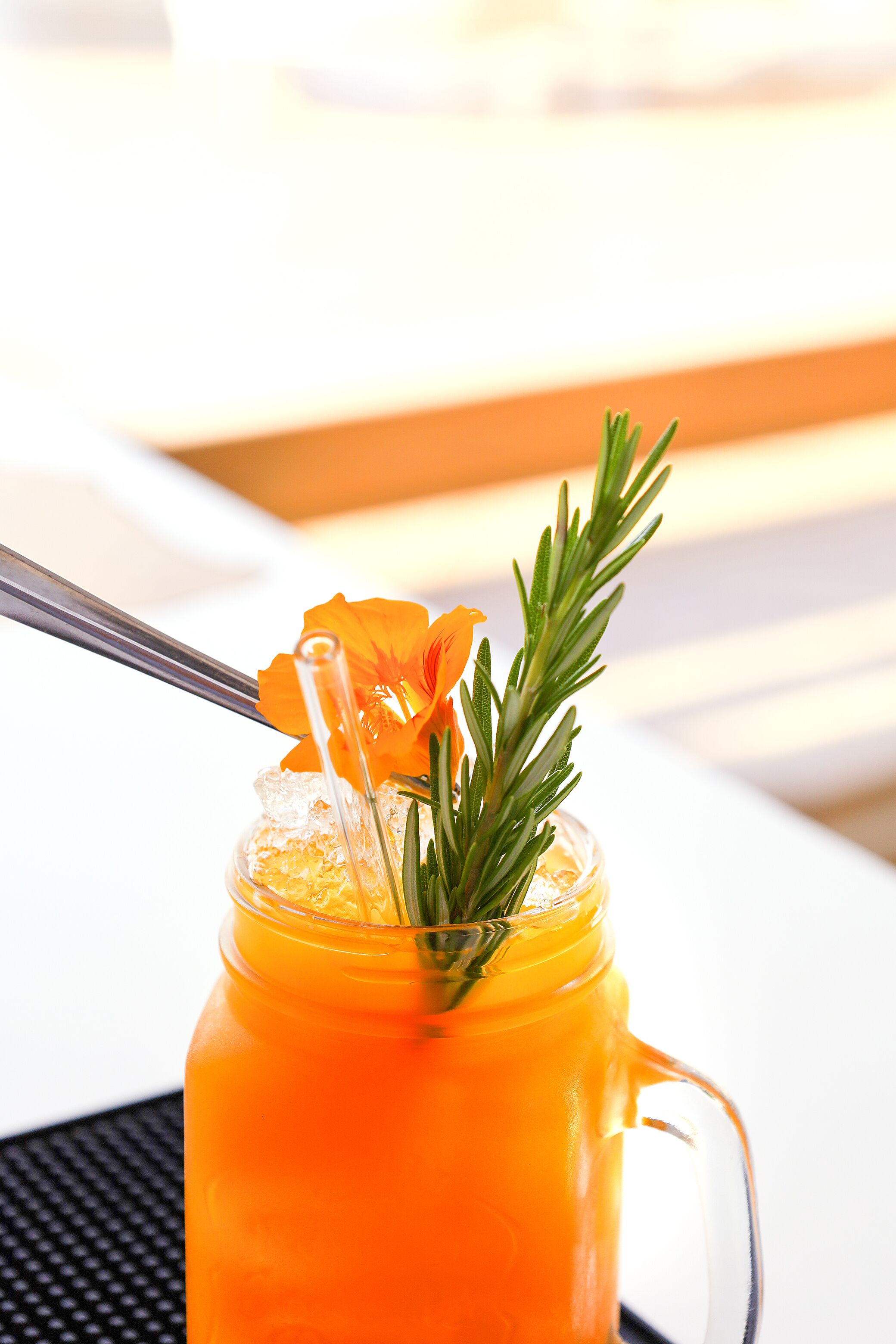 Ein klares Glas mit Henkel, gefüllt mit einer leuchtend orangefarbenen Flüssigkeit, und ein Rosmarinzweig.