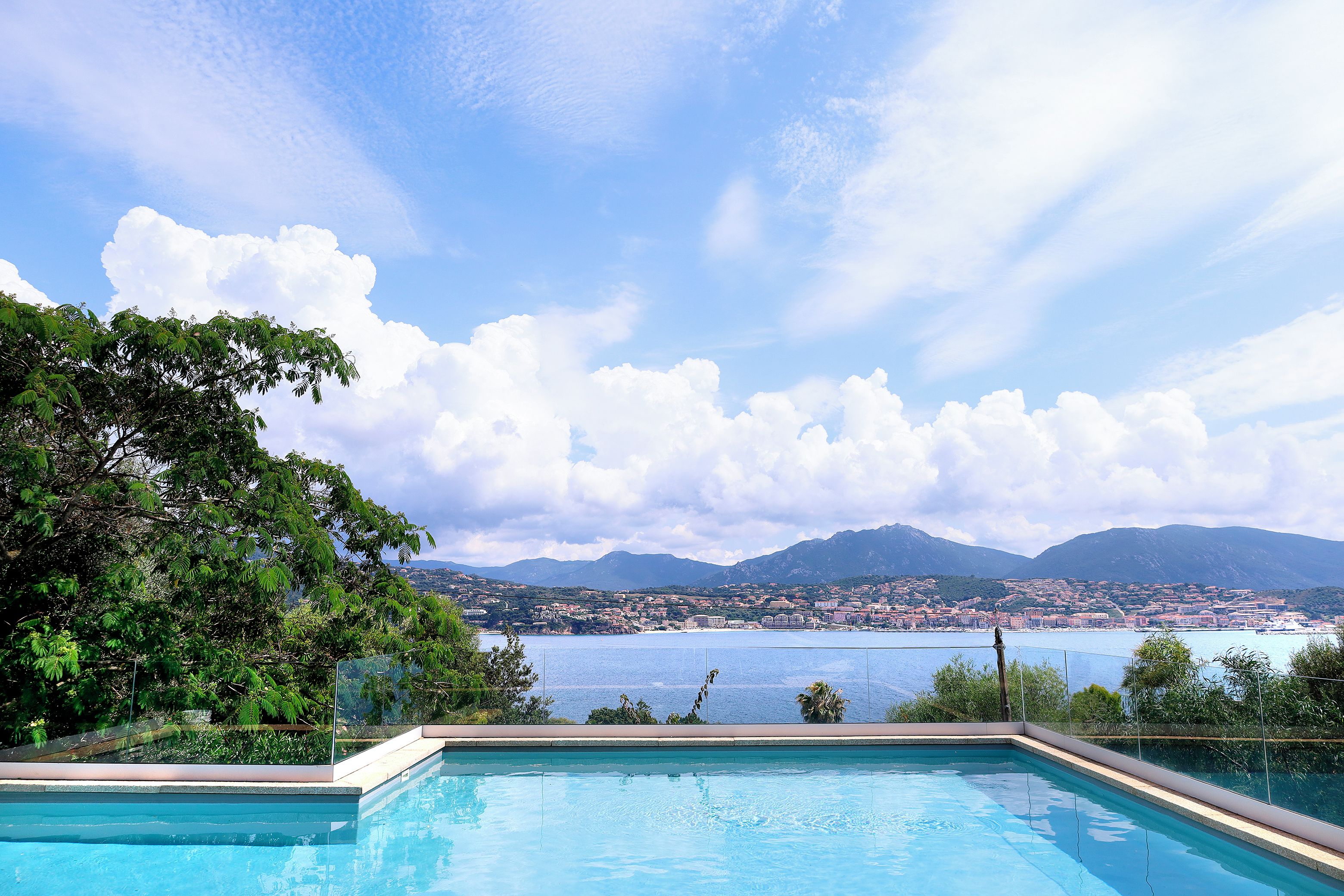 Une piscine offrant une vue dégagée sur une ville côtière et sur les montagnes en arrière-plan.