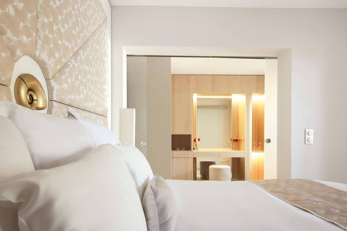 A modern hotel room with a large bed, a bedside table, a mirror, and a view into the bathroom.
