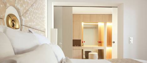 A modern hotel room with a large bed, a bedside table, a mirror, and a view into the bathroom.