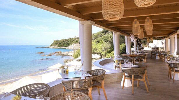 Un espace de restauration en plein air, avec des tables et des chaises en osier, offrant une vue sur une plage et la mer.