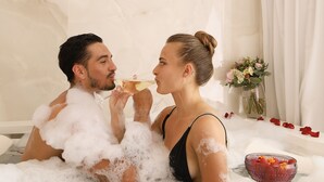 Un couple dans une baignoire remplie de mousse, avec un verre à boire et des pétales de rose.