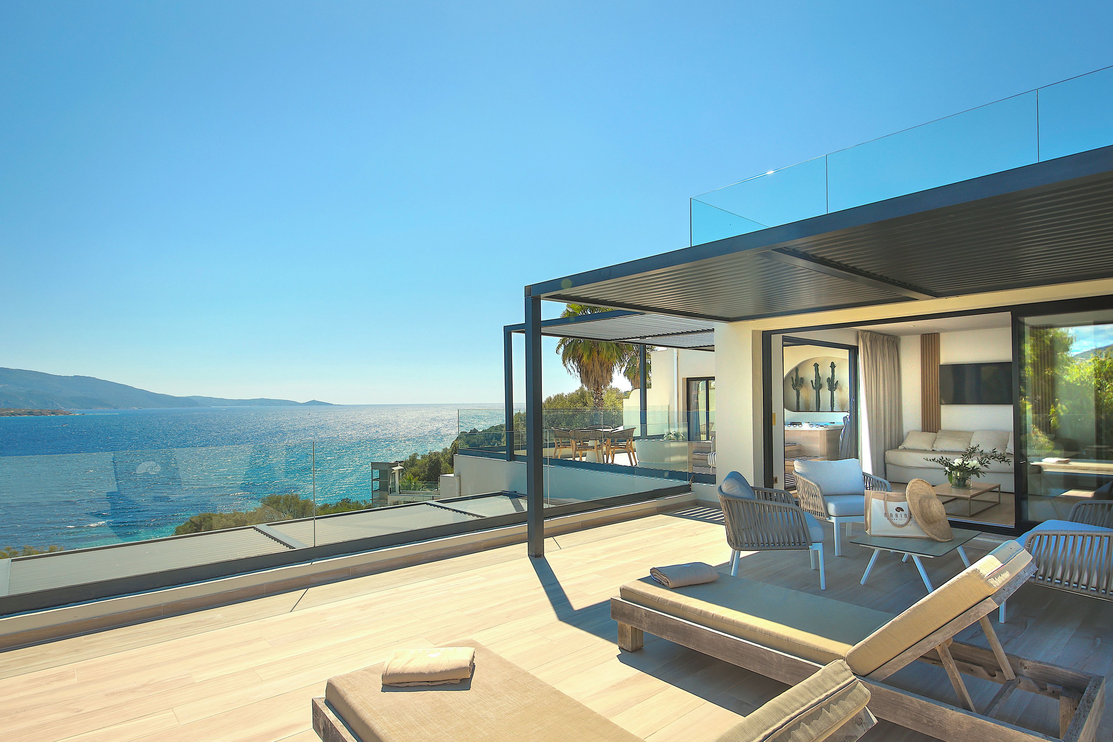 A modern outdoor living space with a pool, lounge chairs, and a view of the sea.