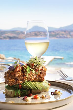 A gourmet dish with a glass of white wine on a plate, set against a scenic seaside backdrop. - Hôtel Marinca & Spa (Olmeto)