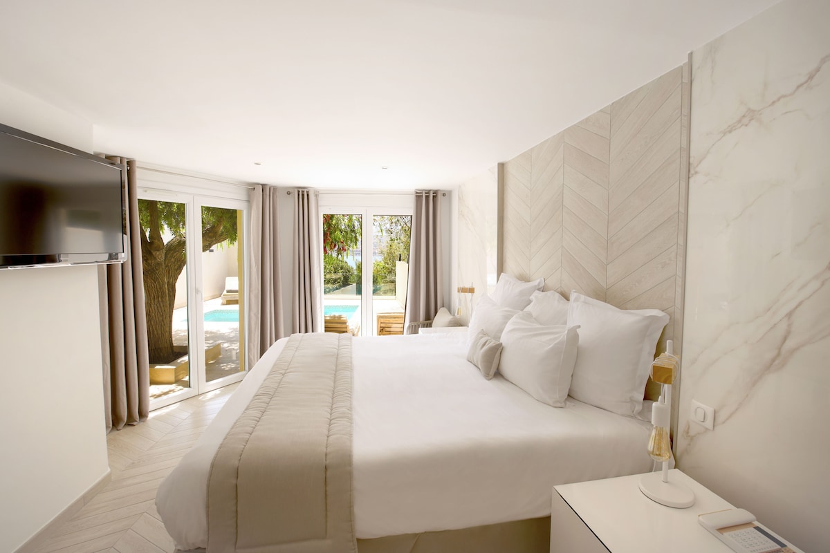 A modern hotel room with a large bed, a TV, and a view of a pool.