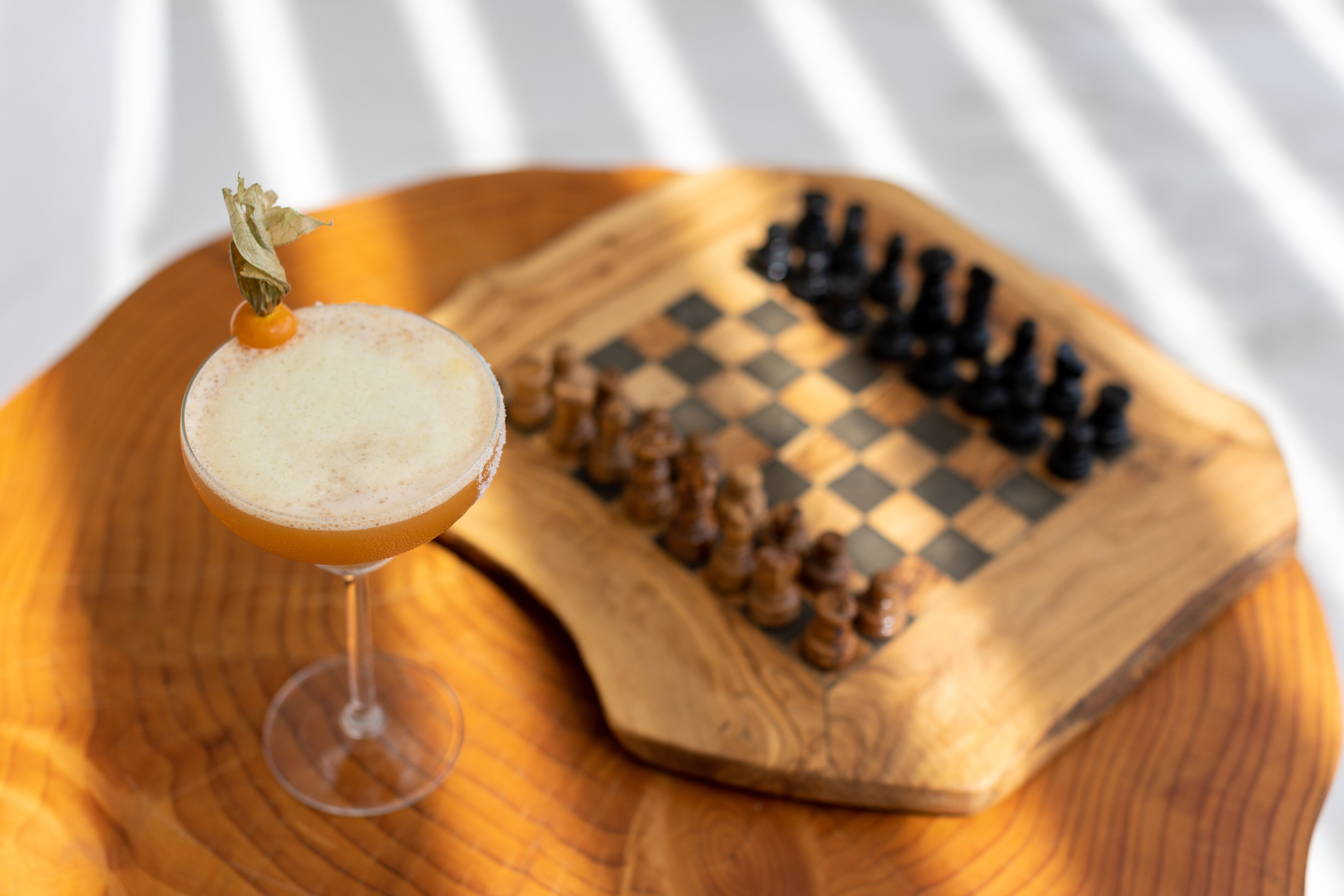 A wooden board with a chess set and a cocktail glass with a garnish.