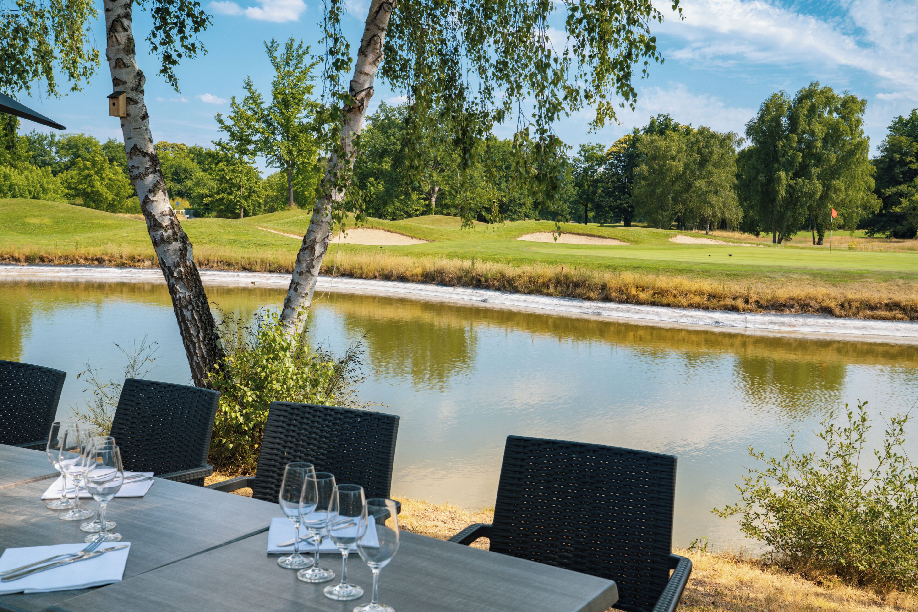Una mesa de comedor con sillas y copas de vino, con vista a un estanque y un campo de golf.