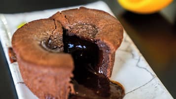Un dessert au chocolat avec une fissure au centre, accompagné de fruits rouges et d’une tranche d’orange, le tout présenté sur une assiette en marbre.