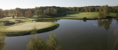 Een golfbaan met een vijver, omgeven door bomen en heldere luchten.